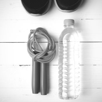 fitness equipment : running shoes,jumping rope and water bottle on white wood table black and white color tone style