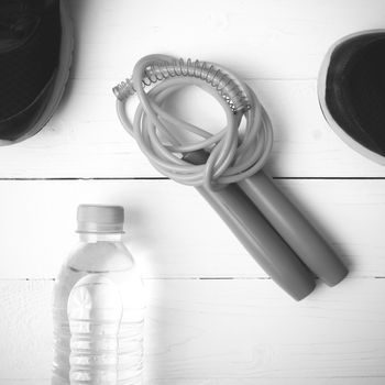 fitness equipment : running shoes,jumping rope and water bottle on white wood table black and white color tone style