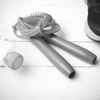 fitness equipment : running shoes,jumping rope and water bottle on white wood table black and white color tone style