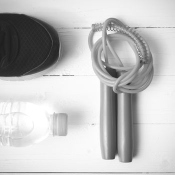 fitness equipment : running shoes,jumping rope and water bottle on white wood table black and white color tone style