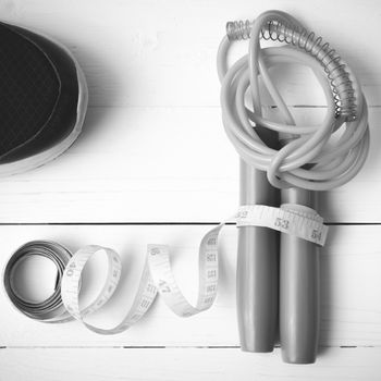 fitness equipment : running shoes,jumping rope and measuring tape on white wood table black and white color tone style