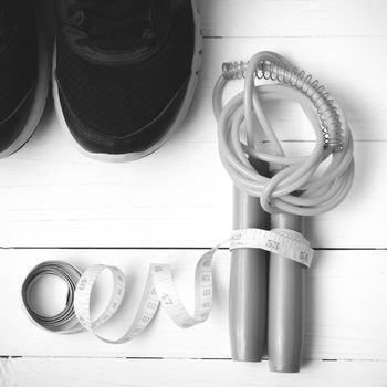 fitness equipment : running shoes,jumping rope and measuring tape on white wood table black and white color tone style