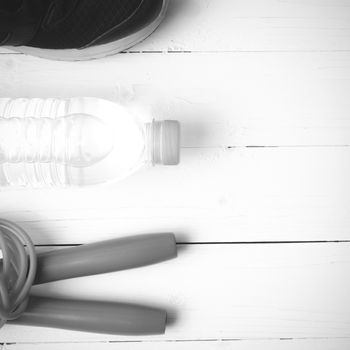 fitness equipment : running shoes,jumping rope and water bottle on white wood table black and white color tone style