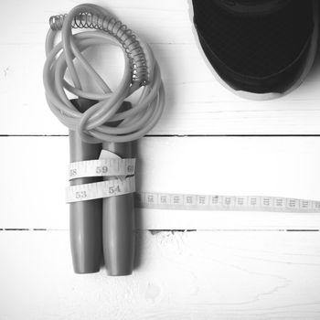 fitness equipment : running shoes,jumping rope and measuring tape on white wood table black and white color tone style