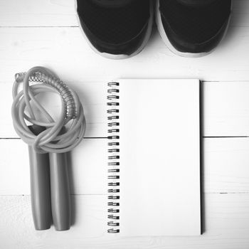 fitness equipment : running shoes,jumping rope and notepad on white wood table black and white color tone style