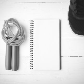 fitness equipment : running shoes,jumping rope and notepad on white wood table black and white color tone style