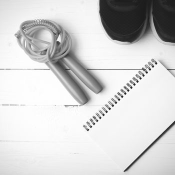 fitness equipment : running shoes,jumping rope and notepad on white wood table black and white color tone style