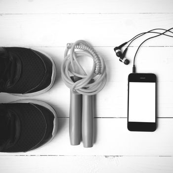 fitness equipment : running shoes,jumping rope and phone on white wood table black and white color tone style