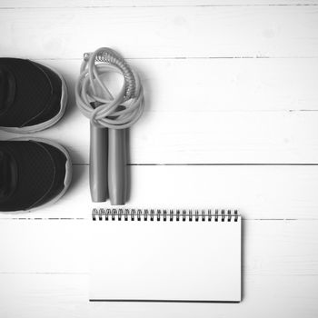 fitness equipment : running shoes,jumping rope and notepad on white wood table black and white color tone style