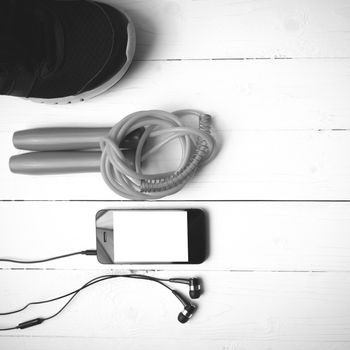 fitness equipment : running shoes,jumping rope and phone on white wood table black and white color tone style