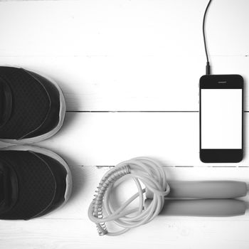 fitness equipment : running shoes,jumping rope and phone on white wood table black and white color tone style