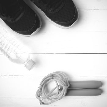 fitness equipment : running shoes,jumping rope, and water bottle on white wood table black and white color tone style