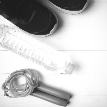 fitness equipment : running shoes,jumping rope,phone and water bottle on white wood table black and white color tone style