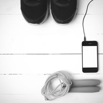 fitness equipment : running shoes,jumping rope and phone on white wood table black and white color tone style