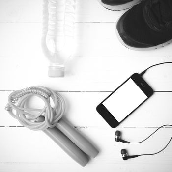 fitness equipment : running shoes,jumping rope,phone and water bottle on white wood table black and white color tone style