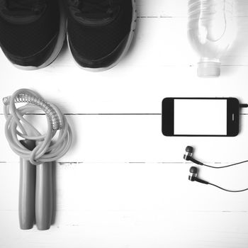 fitness equipment : running shoes,jumping rope,phone and water bottle on white wood table black and white color tone style