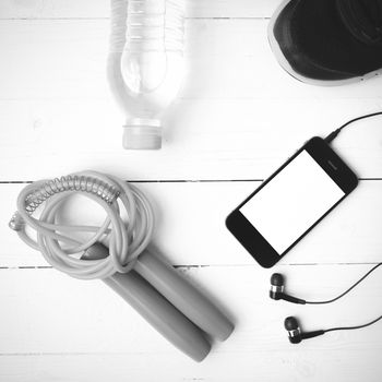 fitness equipment : running shoes,jumping rope,phone and water bottle on white wood table black and white color tone style
