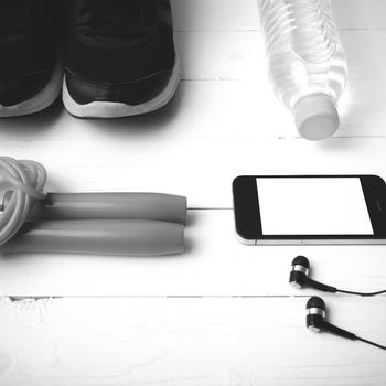 fitness equipment : running shoes,jumping rope,phone and water bottle on white wood table black and white color tone style