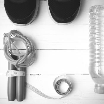 fitness equipment : running shoes,jumping rope,measuring tape and water bottle on white wood table black and white color tone style