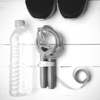 fitness equipment : running shoes,jumping rope,measuring tape and water bottle on white wood table black and white color tone style