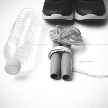 fitness equipment : running shoes,jumping rope,measuring tape and water bottle on white wood table black and white color tone style