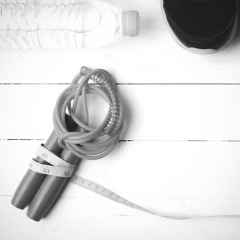 fitness equipment : running shoes,jumping rope,measuring tape and water bottle on white wood table black and white color tone style