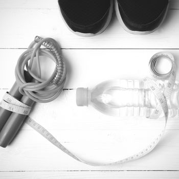 fitness equipment : running shoes,jumping rope,measuring tape and water bottle on white wood table black and white color tone style