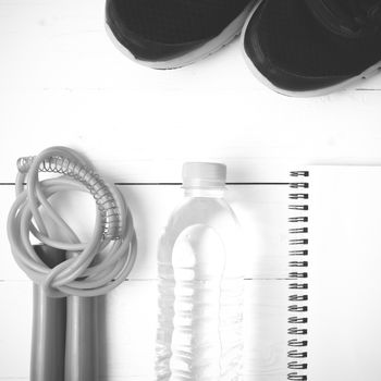 fitness equipment : running shoes,jumping rope,drinking water and notepad on white wood table  black and white tone color style