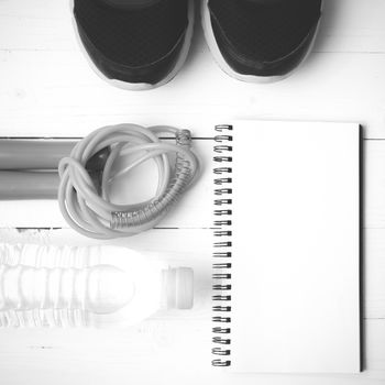 fitness equipment : running shoes,jumping rope,drinking water and notepad on white wood table  black and white tone color style