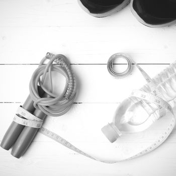 fitness equipment : running shoes,jumping rope,measuring tape and water bottle on white wood table black and white color tone style