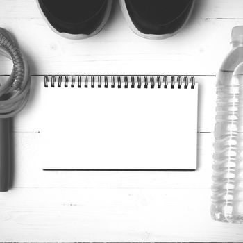 fitness equipment : running shoes,jumping rope,drinking water and notepad on white wood table  black and white tone color style