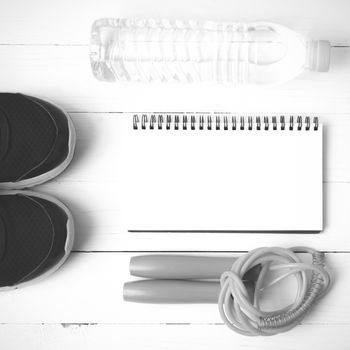 fitness equipment : running shoes,jumping rope,drinking water and notepad on white wood table  black and white tone color style