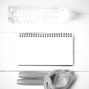 fitness equipment : jumping rope,drinking water and notepad on white wood table  black and white tone color style