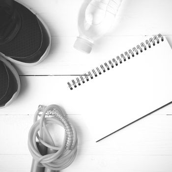 fitness equipment : running shoes,jumping rope,drinking water and notepad on white wood table  black and white tone color style