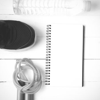 fitness equipment : running shoes,jumping rope,drinking water and notepad on white wood table  black and white tone color style