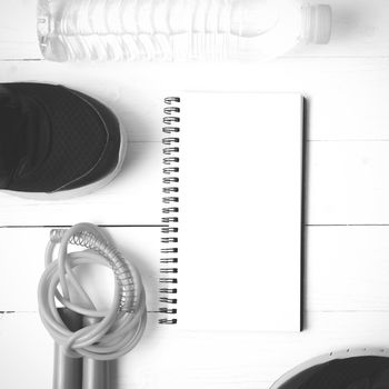 fitness equipment : running shoes,jumping rope,drinking water and notepad on white wood table  black and white tone color style