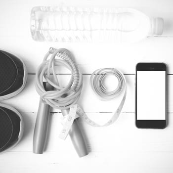 fitness equipment : running shoes,jumping rope,drinking water,measuring tape and phone on white wood table  black and white tone color style