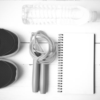 fitness equipment : running shoes,jumping rope,drinking water and notepad on white wood table  black and white tone color style