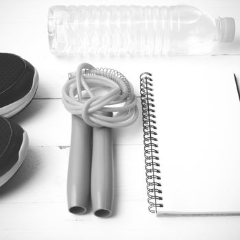 fitness equipment : running shoes,jumping rope,drinking water and notepad on white wood table  black and white tone color style