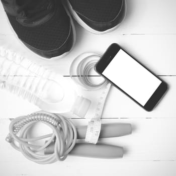 fitness equipment : running shoes,jumping rope,drinking water,measuring tape and phone on white wood table  black and white tone color style