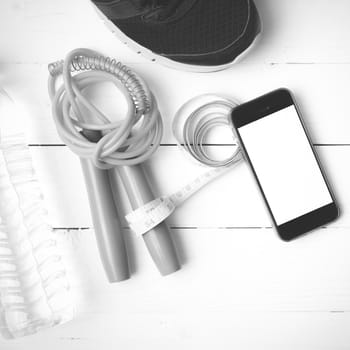 fitness equipment : running shoes,jumping rope,drinking water,measuring tape and phone on white wood table  black and white tone color style