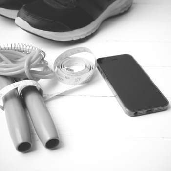 fitness equipment : running shoes,jumping rope,measuring tape and phone on white wood table  black and white tone color style