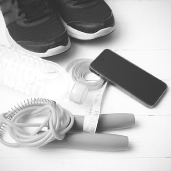 fitness equipment : running shoes,jumping rope,drinking water,measuring tape and phone on white wood table  black and white tone color style