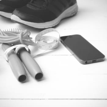 fitness equipment : running shoes,jumping rope,measuring tape and phone on white wood table  black and white tone color style