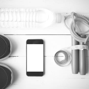 fitness equipment : running shoes,jumping rope,drinking water,measuring tape and phone on white wood table  black and white tone color style