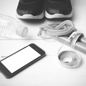 fitness equipment : running shoes,jumping rope,drinking water,measuring tape and phone on white wood table  black and white tone color style