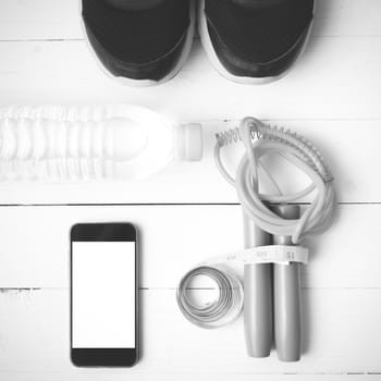 fitness equipment : running shoes,jumping rope,drinking water,measuring tape and phone on white wood table  black and white tone color style