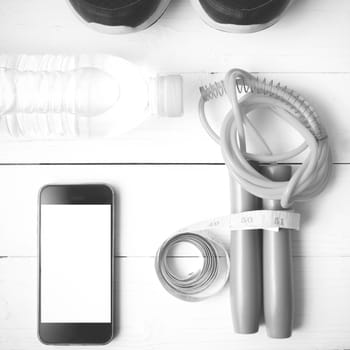 fitness equipment : running shoes,jumping rope,drinking water,measuring tape and phone on white wood table  black and white tone color style