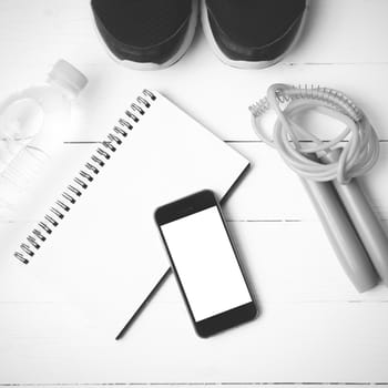 fitness equipment : running shoes,jumping rope,drinking water,notebook and phone on white wood table  black and white tone color style