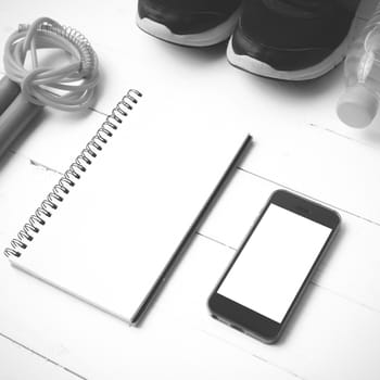 fitness equipment : running shoes,jumping rope,drinking water,notebook and phone on white wood table  black and white tone color style